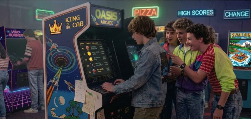 Kids gathered around an Oasis Arcade cabinet in an 80s arcade, its high-score screen reading Wormhole Beacon, Oasis Island